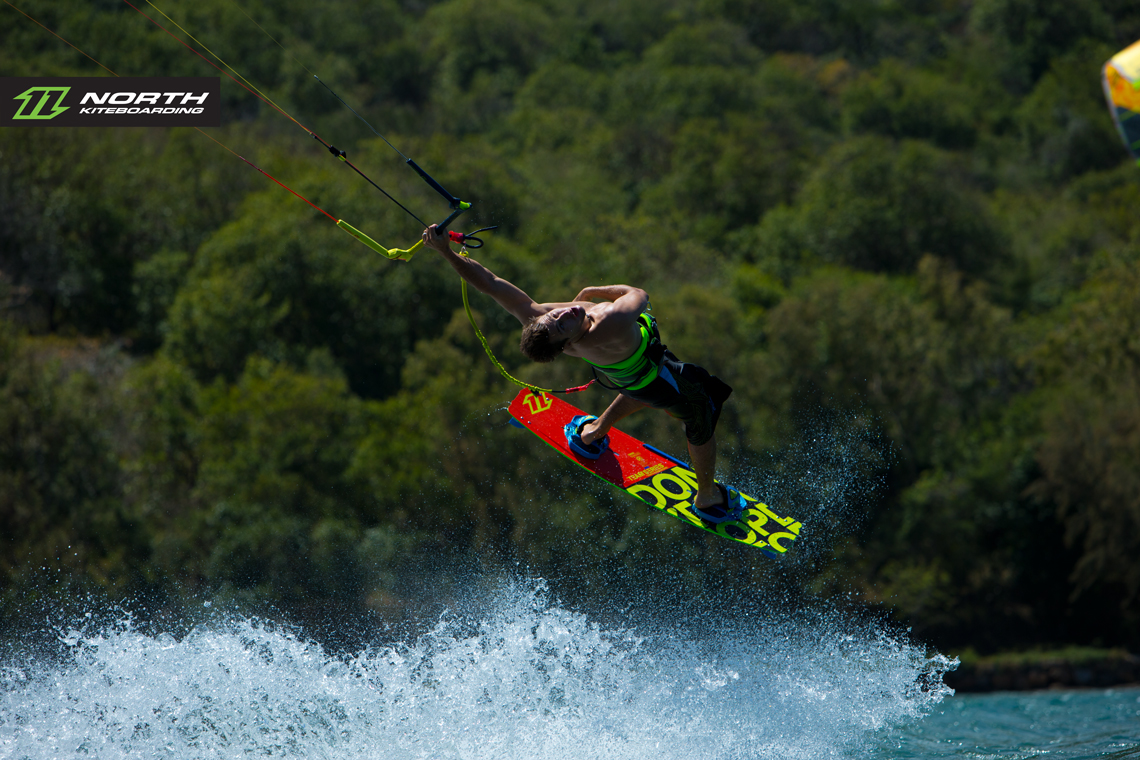 Tom Hebert swinging on one arm and riding the 2015 North Team Series - North kiteboarding