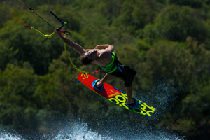 Tom Hebert swinging on one arm and riding the 2015 North Team Series - North kiteboarding